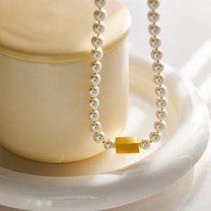 Minimalist pearl necklace with a 18k gold matte metallic bead on white porcelain tray