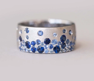 Detailed macro view of matte silver wide band ring with clustered blue gradient gemstones