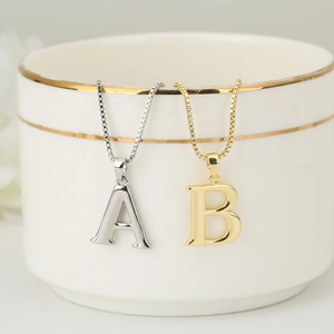 Elegant gold and silver letter A and B pendant necklaces hanging on a white ceramic cup