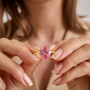 Close-up of a large oval pink topaz gemstone set in a four-prong gold ring on a hand