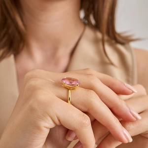 Detail of elegant gold ring featuring a large oval-cut pink gemstone on a model's hand