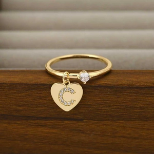 Detail eines goldfarbenen Rings mit rundem Zirkon und Herzanhänger mit Buchstabe C