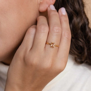 Close-up of square champagne zircon ring with gold band worn on woman's finger