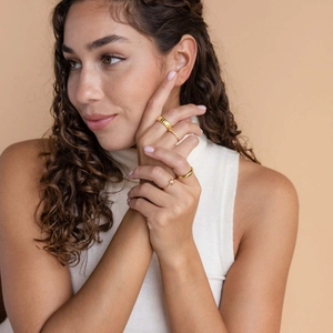 Detail shot of four stacked gold rings with a square pink zircon on a model hand
