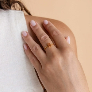 Close-up of a square cut amber zircon ring on a finger with a delicate gold band