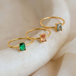 Detailed macro view of three gold rings with emerald-cut emerald, amber, and moss agate stones