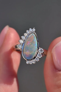 Macro shot of a teardrop-shaped opal ring featuring a colorful play-of-color and side diamonds
