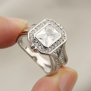 Macro shot of silver ring with emerald cut clear gemstone and halo setting on finger