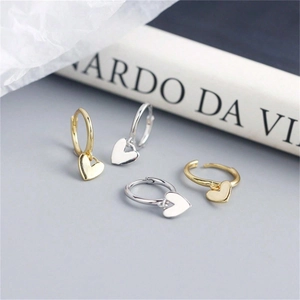 Close-up of gold and silver heart drop earrings on a minimalist artistic background