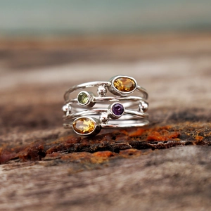 Dettaglio macro di un anello in argento multistrato con gemme colorate su legno antico