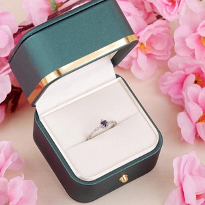 Elegant silver ring with round purple gemstone and diamonds in a green jewelry box