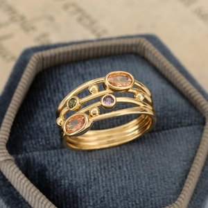 Dettaglio macro di un anello bohémien dorato con pietre arancioni e viola
