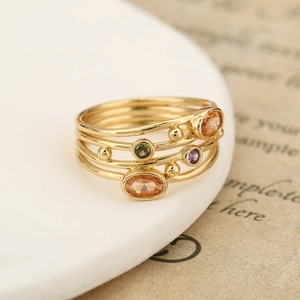 Anello bohémien dorato con gemme arancioni, verdi e viola su ceramica bianca decorata