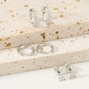 Detailed set of silver clover flower earrings and diamond-encrusted hoops on stone