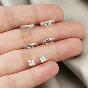 Detailed set of silver clover earrings and crystal studs held by hand on silk cloth