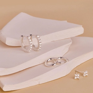 Macro detail of S925 sterling silver clover earrings and diamond hoop set on plaster