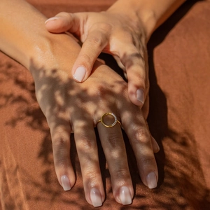 Close-up of golden hollow round ring with sparkling white zircon stones on a model's hand