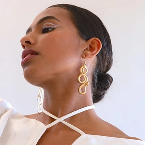 Macro side view of a gold snake-shaped dangle earring worn by a model