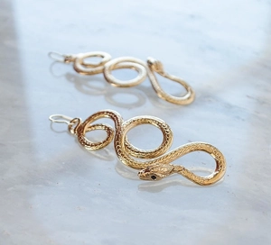Macro view of gold snake earrings showing detailed scales and black gemstone eyes