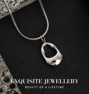 Close-up of silver hollow teardrop pendant on snake chain over black leather background