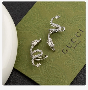 Macro detail of silver dragon ear cuff with pavé crystals on a green background