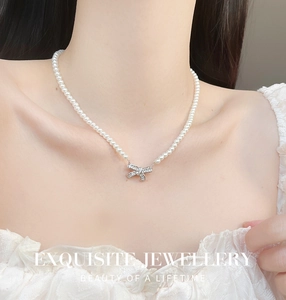 Detailed view of elegant bow pendant with zircons on a white pearl necklace worn by model