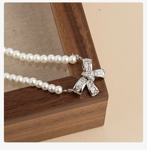 Close-up of pearl necklace with a silver bow pendant featuring baguette-cut zircon
