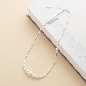 Minimalistische zilveren kralenketting met zeven verloop parels op getextureerde achtergrond