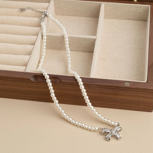 Elegant pearl necklace with silver bow pendant set on a wooden jewelry box