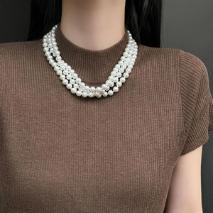 Elegant triple-strand pearl necklace in vintage style worn on a brown knit sweater