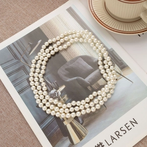 Three-layer long pearl necklace displayed on an artistic book with vintage aesthetic