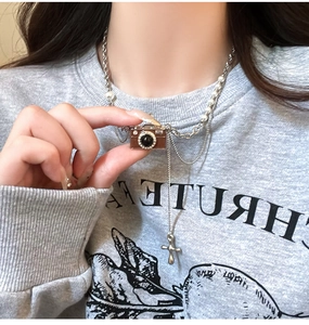 Dettaglio dei ciondoli a fotocamera retrò e croce d'argento su collana di perle