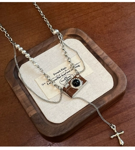Dettagli del ciondolo fotocamera vintage e croce sulla collana di perle a strati