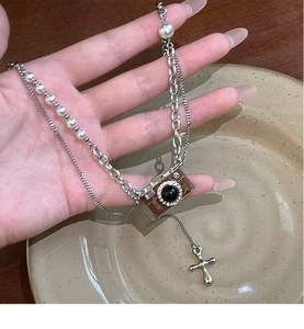 Dettaglio della collana a strati con ciondolo fotocamera vintage, perle e croce