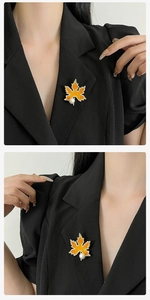 Détail de la broche feuille d'érable en émail orange, dorure et perle sur un revers noir