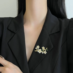 Elegant gold flower brooch with white petals and pearls pinned on a black suit lapel