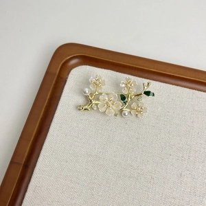 Elegant gold flower brooch with white petals, pearls and green leaves on display
