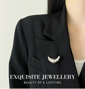 Detailed close-up of a silver croissant-shaped brooch on a black blazer lapel
