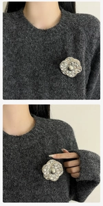 Vue détaillée de la broche camélia avec cristaux et perle sur un pull gris