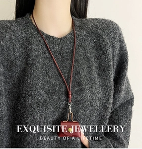 Détail d'un pendentif mini sac en cuir marron rouge sur un pull en maille grise