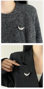 Detailed macro view of the silver croissant-shaped brooch pinned on a knitted fabric
