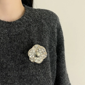 Broche camélia exagérée avec strass et perle grise sur un vêtement en maille