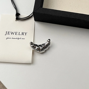 Silver metallic croissant brooch pin with textured surface on minimalist background