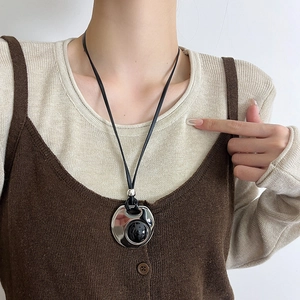 Oval black pendant on leather cord necklace worn over beige sweater, long minimalist jewelry