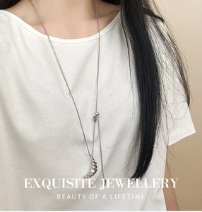Close-up of crescent-shaped silver necklace pendant with elegant ribbed texture on white tee