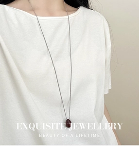 Dettaglio della collana lunga d'argento minimalista con ciondolo a goccia rosso scuro