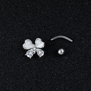 Detailed close-up of a silver butterfly navel ring with opal heart wings on black sand