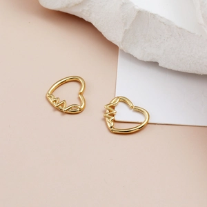 Macro di piercing a cuore dorati con design a linea pulsante su base in pietra