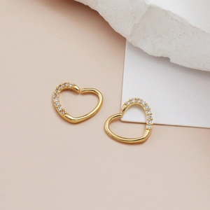 Close-up of golden heart-shaped hoops with micro-set cubic zirconia on cream background