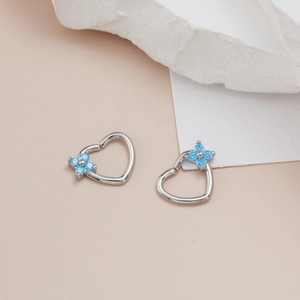 Macro shot of silver heart piercing studs with blue zircon flower on stone background